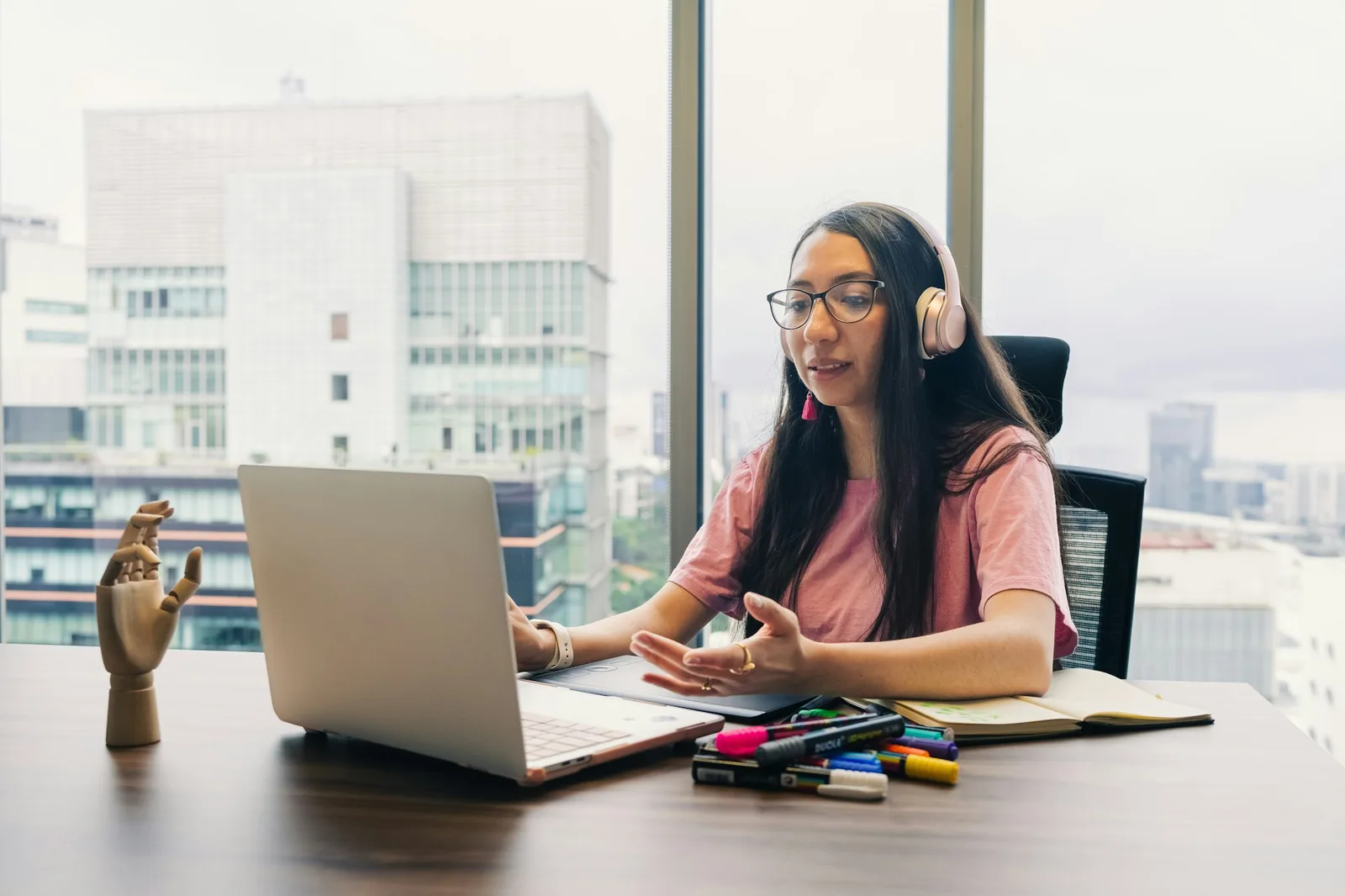 A person in headphones speaking to a laptop by a window